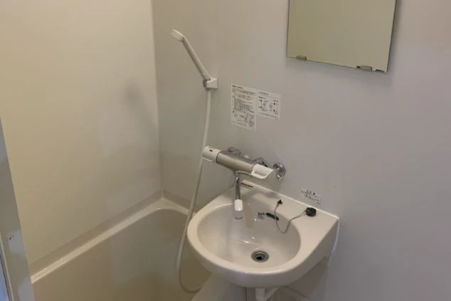 個室内のユニットタイプのバスルームの画像。清潔な浴槽とシャワー、鏡付きの洗面台がコンパクトにまとまった、プライベートを重視した水回り設備。