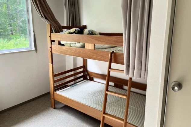 窓があり明るい、木製の二段ベッドが置かれたリゾートバイト寮の個室。