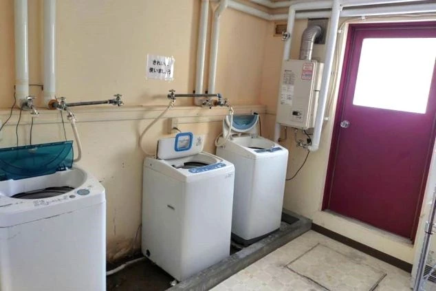 リゾートバイトの寮に備え付けられた洗濯機を撮影した画像。ドラム式ではなく、上から洗濯物を入れる縦型タイプが2台設置されている。リゾートバイトの寮の共用スペースの画像。