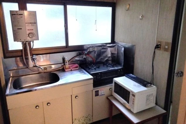 リゾートバイト寮のキッチンの画像。シンク、ガスコンロ、給湯器、電子レンジが完備されており、自炊に便利な設備。