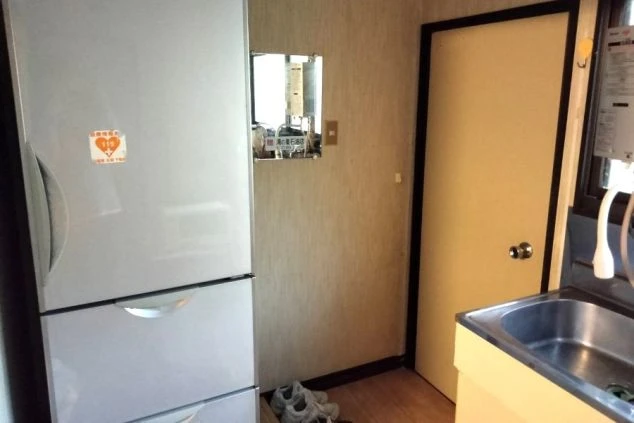 リゾートバイト寮のキッチン設備の画像。大型の冷蔵庫とキッチンシンク、室内ドアが見えており、自炊可能な環境が整っている。