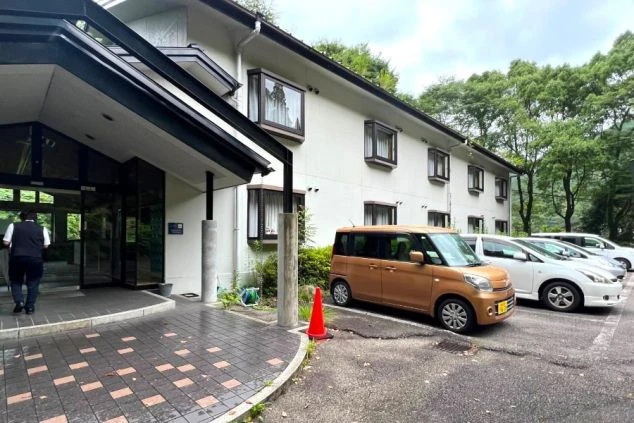 客室を利用するリゾートバイト寮の建物外観画像。社員寮としても使われるホテル風の建物で、駐車場もあり、周辺は自然に囲まれている。