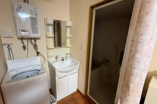 寮の洗面・洗濯スペース。洗面台、洗濯機、壁掛け式の給湯器、そしてガラス戸の奥に浴室が見える。