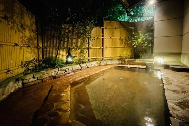 竹垣と石に囲まれた夜の露天風呂の画像。旅館・ホテルでのリゾートバイトの勤務後に入れる温泉の特典イメージ。