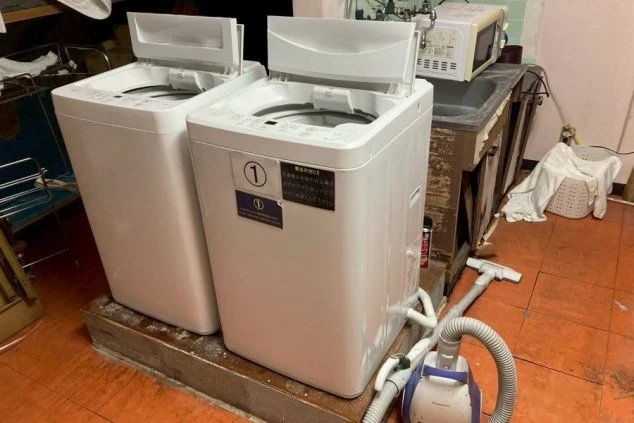 スタッフ寮内のランドリースペース。2台の縦型洗濯機が並び、右奥には流し台と電子レンジがある。