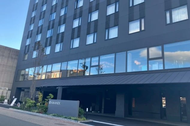 外観。黒い外壁の多層階の建物で、下層階はガラス窓と車寄せの庇（ひさし）になっている。