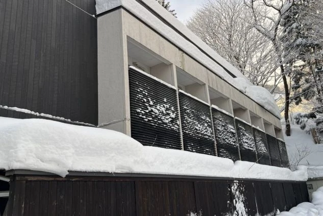 スタッフ寮の外観画像。深い雪に包まれた冬の風景と、モダンで堅牢な造りの居住棟。