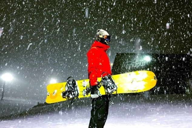 雪が激しく降る中、スノーボードを持つ人。リゾートバイトは、最高の雪質を満喫できます。