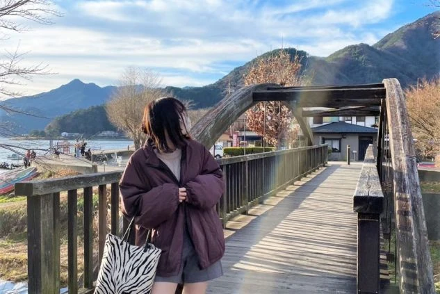 穏やかな湖と山を背景に、橋の上で景色を眺めている女性。リゾートバイトの休日の様子。