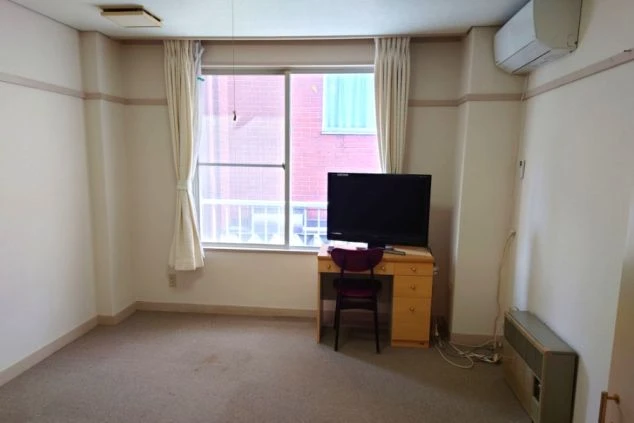 寮の個室内部。エアコン、テレビ、デスク、窓があり、明るくゆとりのある部屋。