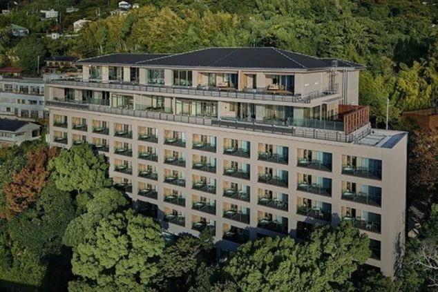 緑豊かな山腹にある、モダンな外観の複数階建てのホテルまたは旅館。