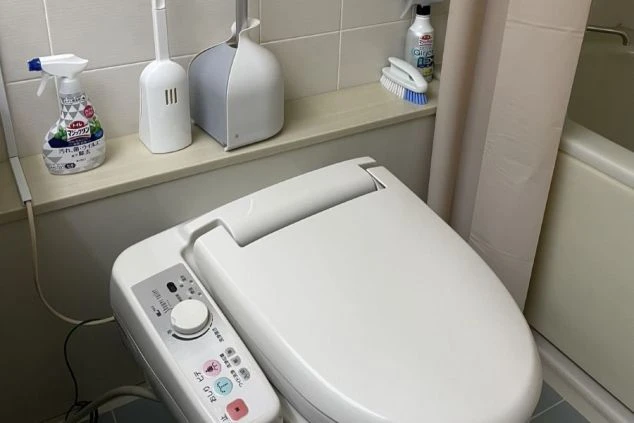 日本のモダンなバスルームのクローズアップで、温水洗浄便座が特徴です。便座の側面には、洗浄機能や温度などを操作するためのパネルが見えます。