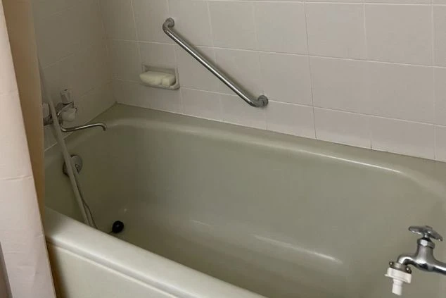 薄暗い照明のバスルームのクローズアップで、水が流れる様子を想像させます白い浴槽とその上にある銀色の蛇口が特徴です。蛇口は現代的なデザインで