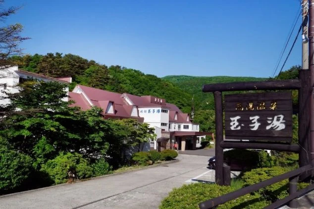 温泉の看板が目立つ、緑豊かな山々に囲まれた玉子湯旅館の外観。