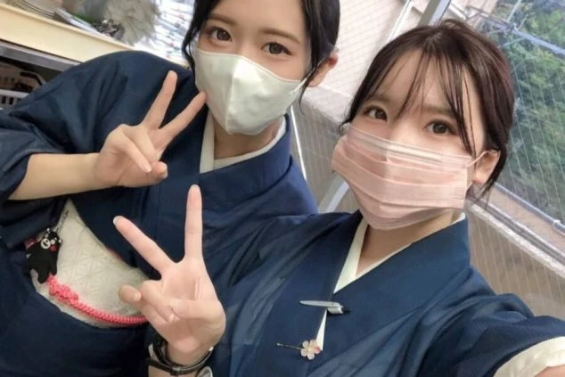 リゾートバイトのスタッフの女性2人が、和装の制服にマスク姿でピースサインをする笑顔の自撮り写真。和風旅館や温泉地での求人イメージ。