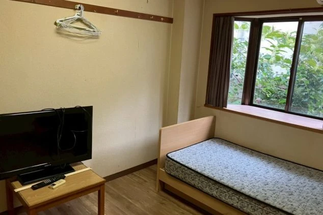 リゾートバイトの寮の部屋の中を撮影した画像。部屋にはベッドとテレビ、そして窓が写っている。リゾートバイトの寮の部屋の画像。