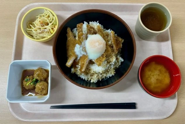 リゾートバイトのまかない画像。チキンカツ丼と、サラダ、スープ、お茶がセットになった食事。