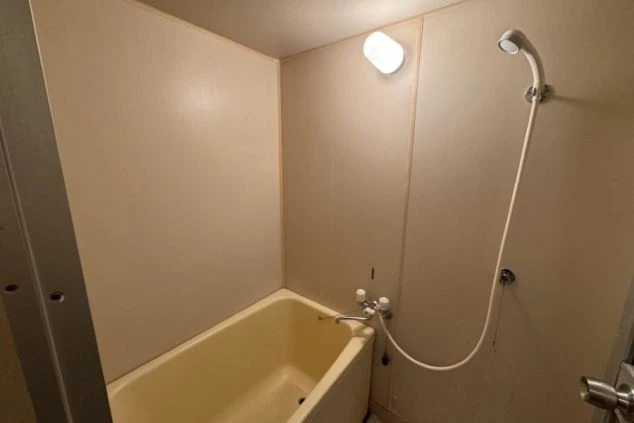 寮の浴室。ベージュ色のユニット式の浴槽と壁で、シャワーと照明が設置されている。