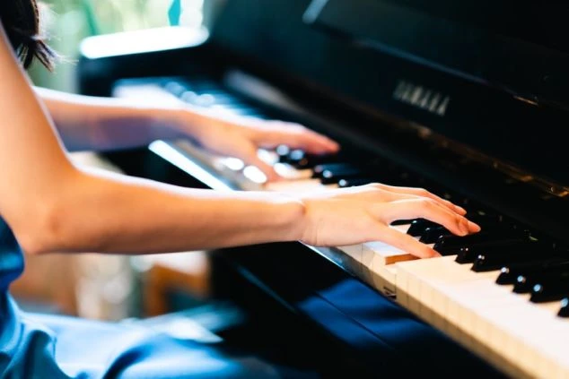 黒いアップライトピアノを演奏する人の手元がクローズアップされた写真。ピアニストのリゾートバイトの仕事イメージ。