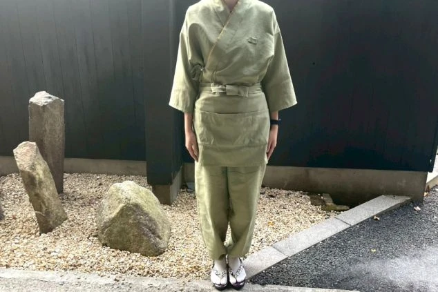 和風旅館の作務衣制服（女性用）。緑がかったベージュ色の作務衣とエプロン。