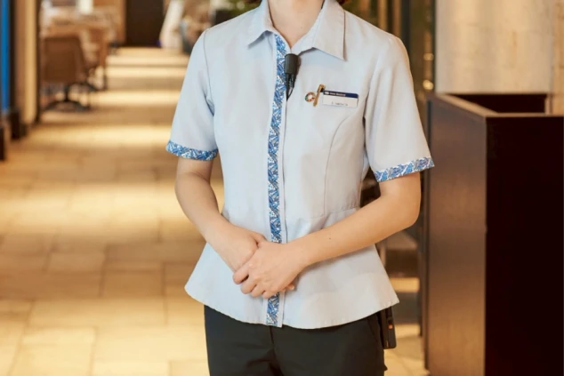 女性スタッフの制服。薄い水色のシャツに、胸元と袖口に青い沖縄柄のアクセントが入っている。シャツはウエストが絞られたデザイン。
