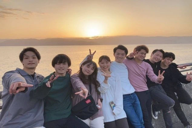 夕焼けの海辺でポーズをとるリゾートバイトの仲間たち。集合写真、友達との思い出。