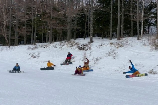 雪の斜面に座り込んだり寝転んだりして、スノーボードを楽しむリゾートバイト仲間たちの集合写真のワクトリオリジナル画像。
