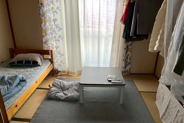 リゾートバイトの寮の寝室。フローリングの床に布団が敷かれており、デスクと大きな窓がある明るい洋室。