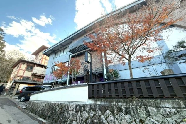 石垣と黒い塀の奥に建つ、グレーの壁と煉瓦調の入り口が特徴的な和風建築の宿泊施設。