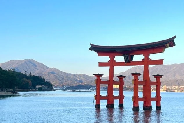 水面に浮かぶ朱色の大きな鳥居。背景には山々の稜線と青い空が広がる。
