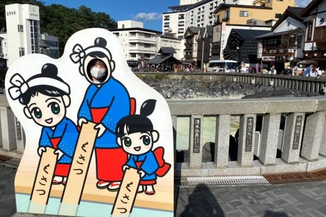 群馬県草津温泉の湯畑前で湯もみ娘の顔出しパネルを楽しむワクトリスタッフの画像。