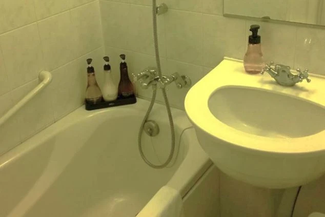 従業員寮のユニットバス。白い浴槽と、洗面台が一体となった構造。シャンプーなどのボトルが置かれ、壁に手すりがある。