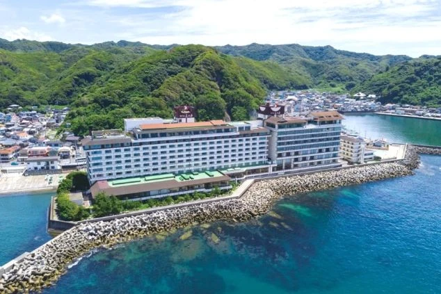 海沿いの岩場に建つ、複数の建物からなる大型ホテル。背景には緑豊かな山々が広がる。