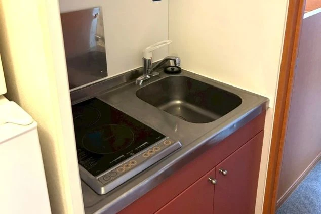 従業員寮のミニキッチン。冷蔵庫の上に電子レンジが置かれており、奥には居室のドアが見える。