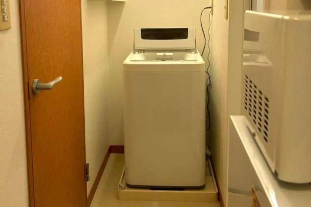従業員寮の洗濯スペース。廊下の奥まった場所に白い縦型洗濯機が置かれている。