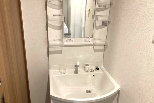 清潔感のある白の洗面化粧台。鏡の左右にはプラスチックのラックが備え付けられている。