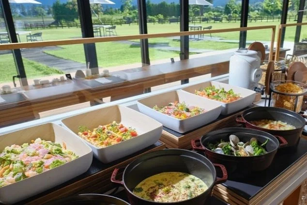 ガラス窓の向こうに芝生が見えるカウンターに、サラダやシチューなどのビュッフェ料理が並ぶ。