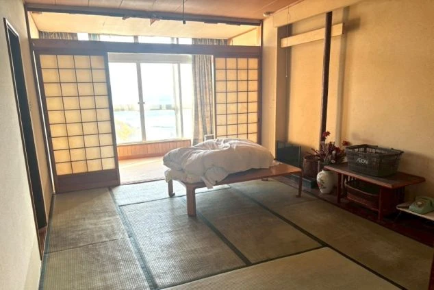 広々とした和室の客室寮。テーブルや布団が用意されており、大きな窓からは明るい陽が差し込んでいる。