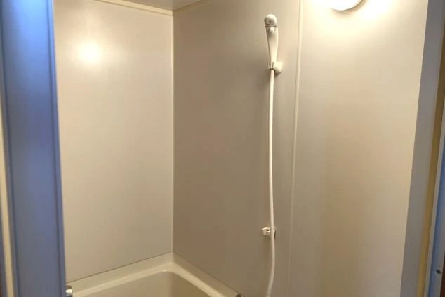 白い壁の浴室。シンプルなシャワーヘッドと蛇口、浴槽の一部が見えるユニットバスの内部。