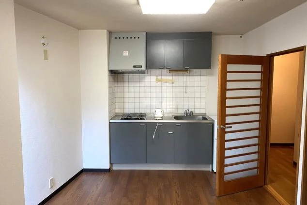 グレーのシステムキッチン。上下に収納棚があり、2口ガスコンロ、電気ケトル、シンクが備わっている。