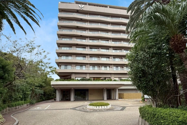 青空の下、大きなヤシの木に挟まれるように建つ、現代的な多層階の大型ホテルの外観。