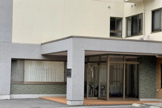 寮の入口。コンクリートの柱とガラスドアで構成されたエントランスで、建物の壁はベージュ色。