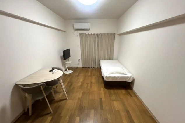 フローリングの床の個室寮。エアコンが設置されており、部屋にはベッド、テレビ、そしてテーブルが置かれている。