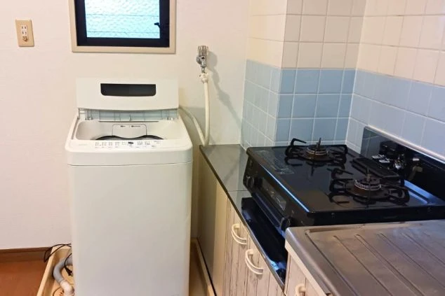 個室内に設置されたシステムキッチンと、すぐ横に用意された全自動洗濯機。自炊や洗濯が室内で完結する、非常に利便性の高いリゾートバイト寮の設備環境。