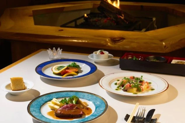 温かみのある囲炉裏を背景に並ぶ、色鮮やかな本格コース料理の画像。リゾートホテルや高級旅館の料飲接客（レストランホール）職種で提供される、こだわりの食事イメージ。