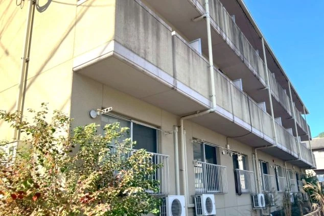 寮として利用される集合住宅の外観。南向きのベランダにはエアコンの室外機が並び、日当たりの良い3階建ての建物。