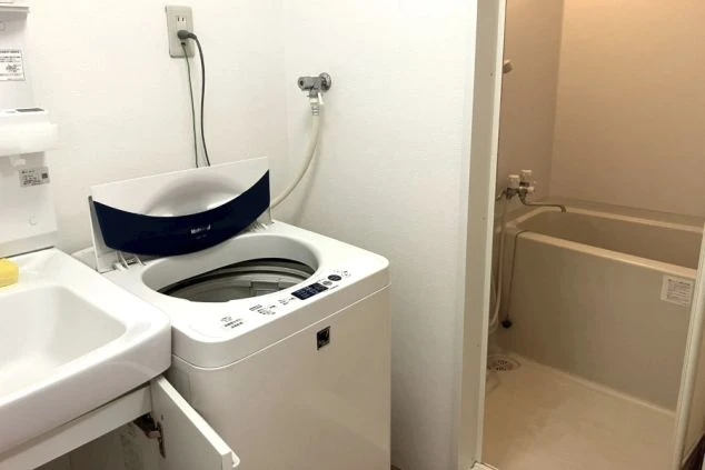 寮の洗面所とバスルーム。全自動洗濯機、洗面台、およびユニットバス形式の浴槽が設置されている。