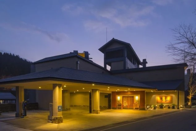 夜のライトアップが美しい温泉旅館の外観。広々とした車寄せと和モダンな玄関口が印象的な建物の全景