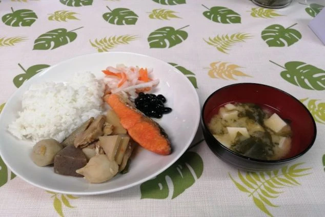 白いご飯、焼き鮭、筑前煮、黒豆、味噌汁がバランス良く並んだ充実しているまかないの画像。