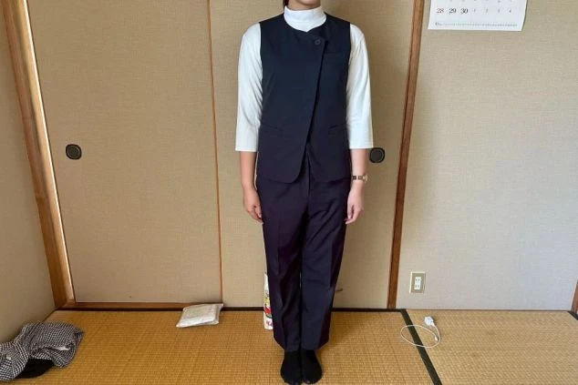 ネイビーのベストとスラックスを合わせたモダンな女性スタッフの制服画像。インナーは白のハイネックで、清潔感のある洗練された装い。
